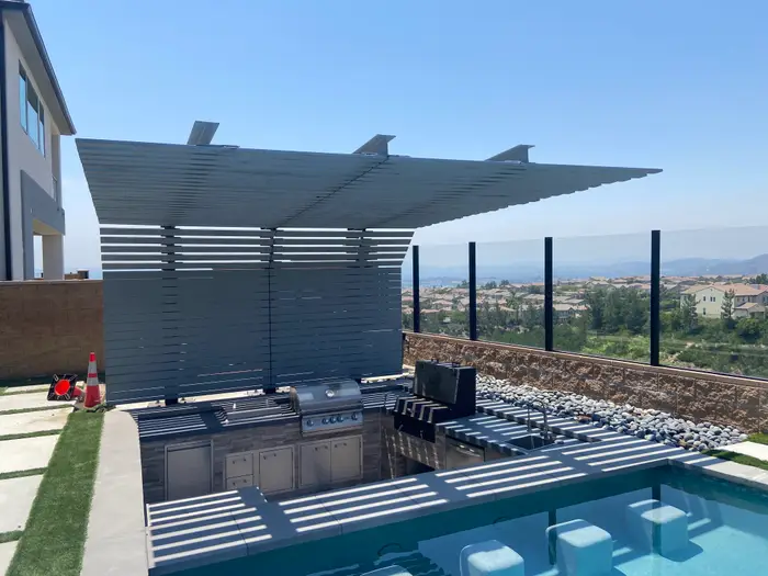Louvered aluminum pergola over an outdoor kitchen beside a pool